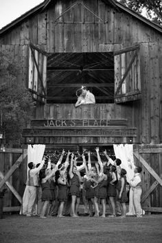 a group of people standing in front of a barn with their hands up to the sky