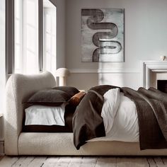 a bed with pillows and blankets on it in front of a window next to a fireplace