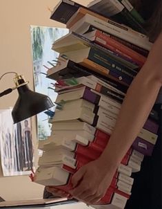 a woman holding a stack of books in front of a desk with a lamp on it