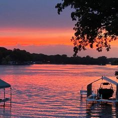 a boat is docked at the end of a lake as the sun sets in the distance