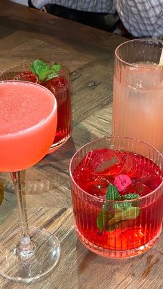 three glasses filled with different types of drinks on top of a wooden table next to each other