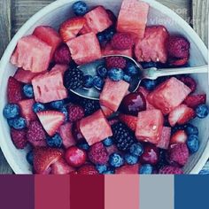 a bowl filled with watermelon, raspberries and blueberries next to a spoon