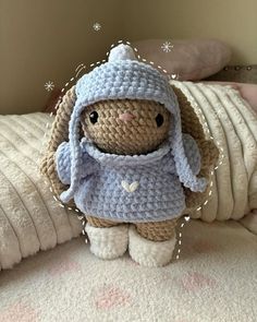 a crocheted stuffed animal wearing a blue hat and sweater on top of a bed