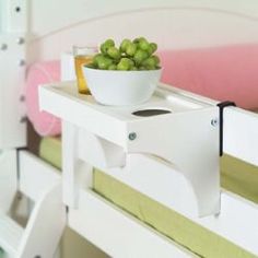 a bowl of green grapes sitting on top of a white table next to a bed