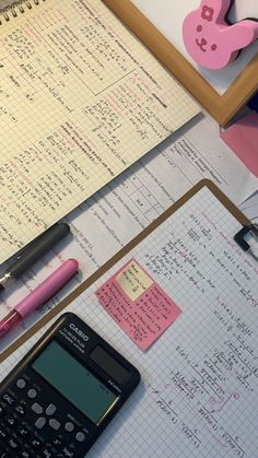 a calculator and pen sitting on top of a notebook next to a cell phone