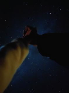 a person's hand reaching up into the sky with stars in the background at night