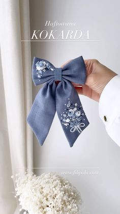 a hand holding a blue bow with white flowers on it and the words kokarda written below