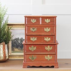 a wooden dresser with gold handles on it next to a potted plant and framed photograph