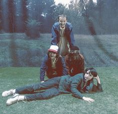 four people are laying on the grass with one person holding his head and another standing behind him