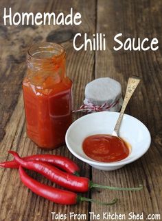 homemade chili sauce in a small white bowl next to two red hot peppers on a wooden table