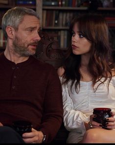 a man and woman sitting next to each other in front of a bookshelf