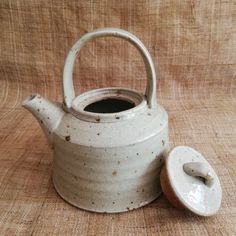 a white tea pot with a lid on a wooden tableclothed surface, next to a cup and saucer