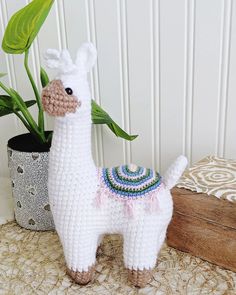 a crocheted white llama next to a potted plant