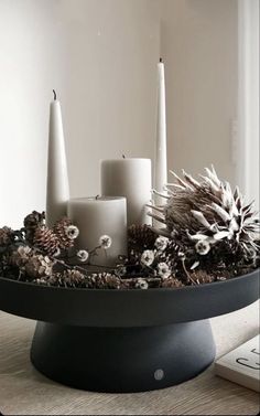 some candles are sitting in a bowl with pine cones and flowers on the table next to a remote control