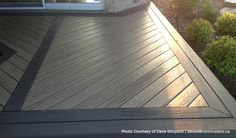 a cat is sitting on the edge of a wooden deck in front of a house