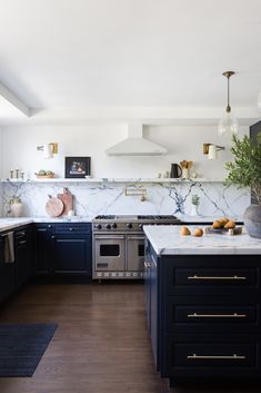 a kitchen with marble counter tops and black cabinets, along with brass pulls on the doors