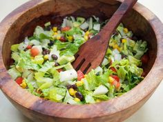 a wooden bowl filled with lettuce, black beans and corn next to a fork