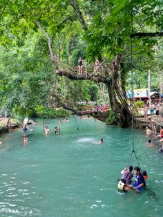 people are swimming in the river while hanging from trees over their heads and swinging on ropes