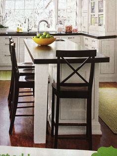 a kitchen with white cabinets and an island in front of the window, has a bowl of fruit on it