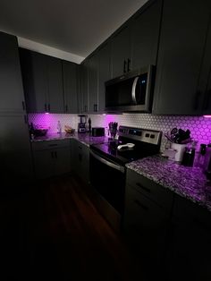 a kitchen with dark cabinets and purple lighting on the counter tops, along with black appliances