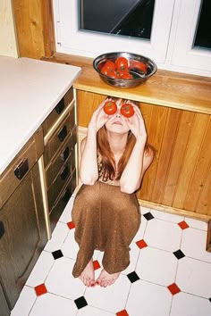 a woman sitting on the floor with tomatoes in front of her eyes