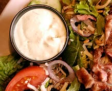 a plate with meat, salad and dressing on it