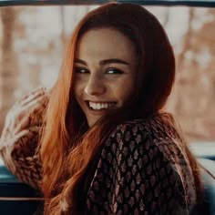 a woman sitting in the back seat of a car with long red hair and smiling