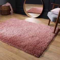 a pink rug on the floor in front of a round mirror with a chair next to it