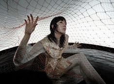 a woman sitting on the ground with her hands up in front of an artistic mesh net