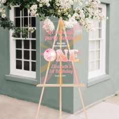 an easel with a sign and flowers in front of a building