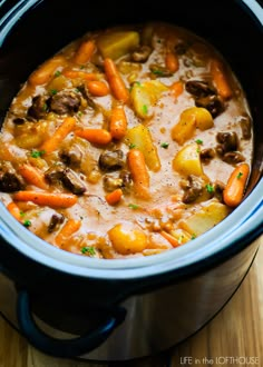 a crock pot filled with stew and carrots on top of a wooden table