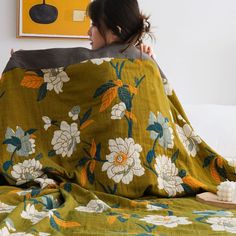 a woman sitting on top of a bed covered in a green floral blanket and pillow