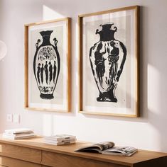 two black and white vases are hanging on the wall above a wooden dresser with books