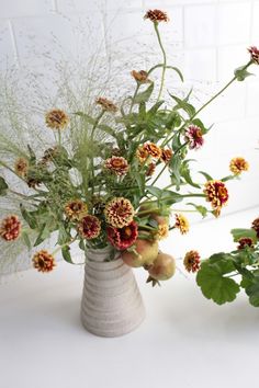 a vase filled with lots of flowers on top of a white table next to plants