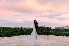 a bride and groom standing on top of a balcony at sunset with the sky in the background