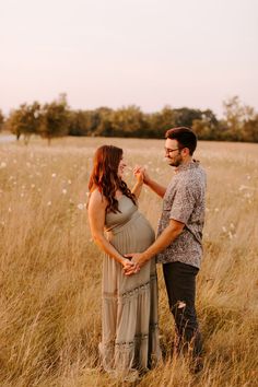 a pregnant woman standing next to a man in a field