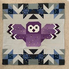 a purple and black quilt with an owl on it's back, sitting on the floor