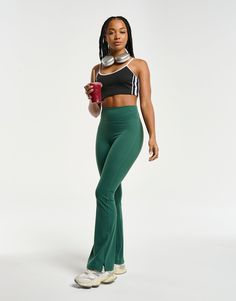 a woman in green pants holding a drink and looking at the camera with one hand on her hip