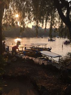 several canoes are docked at the edge of a lake as the sun is setting