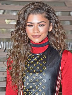 a woman with long curly hair wearing a leather vest