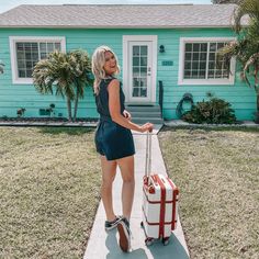 a woman is standing on the sidewalk with her luggage in front of a blue house