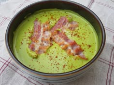 a bowl filled with green soup and bacon pieces on top of the food in it