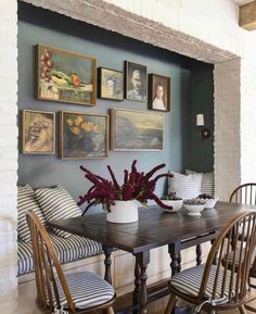 a dining room table with four chairs and pictures on the wall above it, along with vases filled with flowers