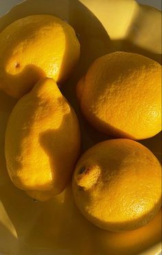 four lemons in a white bowl on a table