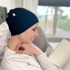 a woman wearing a beanie reading a book on a couch in front of a window