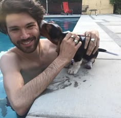 a man holding a small dog in his lap next to a swimming pool and smiling at the camera