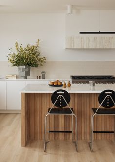 two black chairs sitting in front of a kitchen island with white counter tops and cabinets