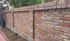 a red brick wall next to a sidewalk and fenced in area with trees on the other side