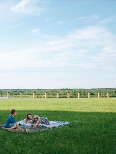 two people sitting on a blanket in the grass