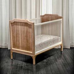 a white crib with wooden slats in front of a curtained wall and floor